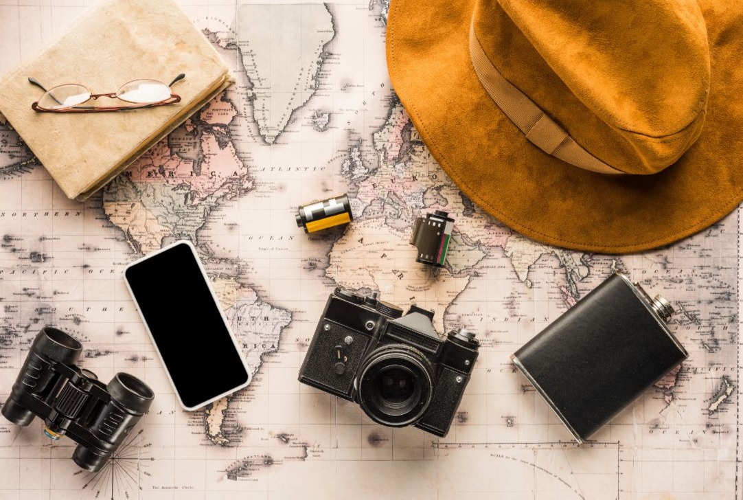 Multimedia camera objects placed on a map together with a hat and notebook representing tourism and its environmental impact