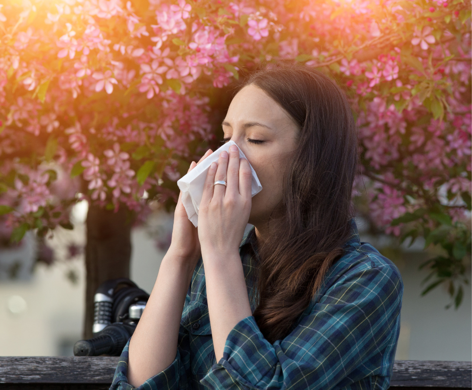 Inquinamento e allergie si combinano con l'immagine di una ragazza circondata da fiori che si soffia il naso